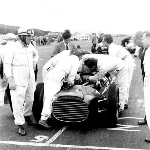 Reg Parnell, left, waits on the grid at Turnberry Circuit in 1952 whilst the BRM Mechanics work on the complex CRM V16 grand prix car.