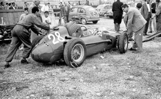 Enzo Ferrari’s old friend and chief mechanic Luigi Bazzi steers the brand new Ferrari Dino grand prix car as it is pushed through the unsurfaced paddock behind the pits