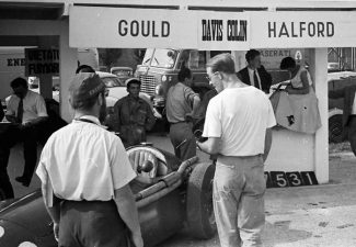 Famed English racing journalist the bearded Denis Jenkinson with privateer Bruce Halford in the pits. Note the slapdash way the drivers name cards have been printed.