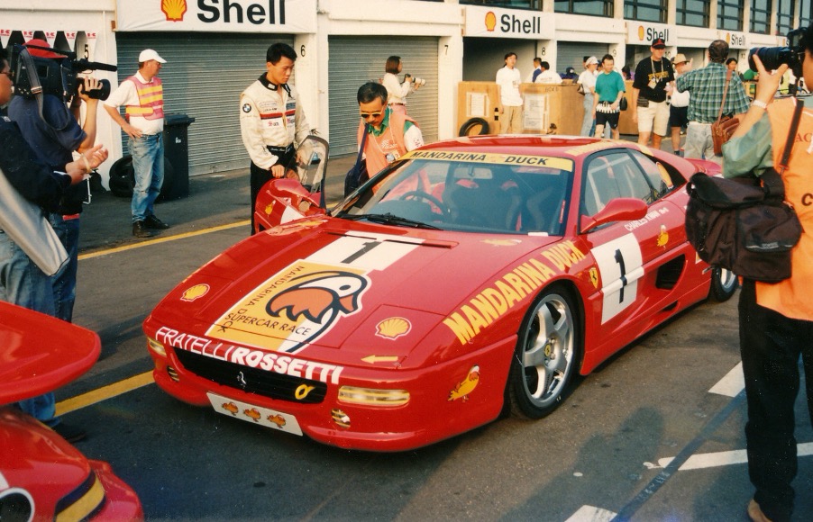 A person standing in front of a red car

Description automatically generated