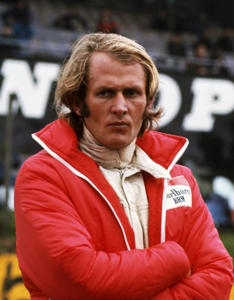 Helmut Marko, a racing driver, in white overalls with red jacket not smiling
