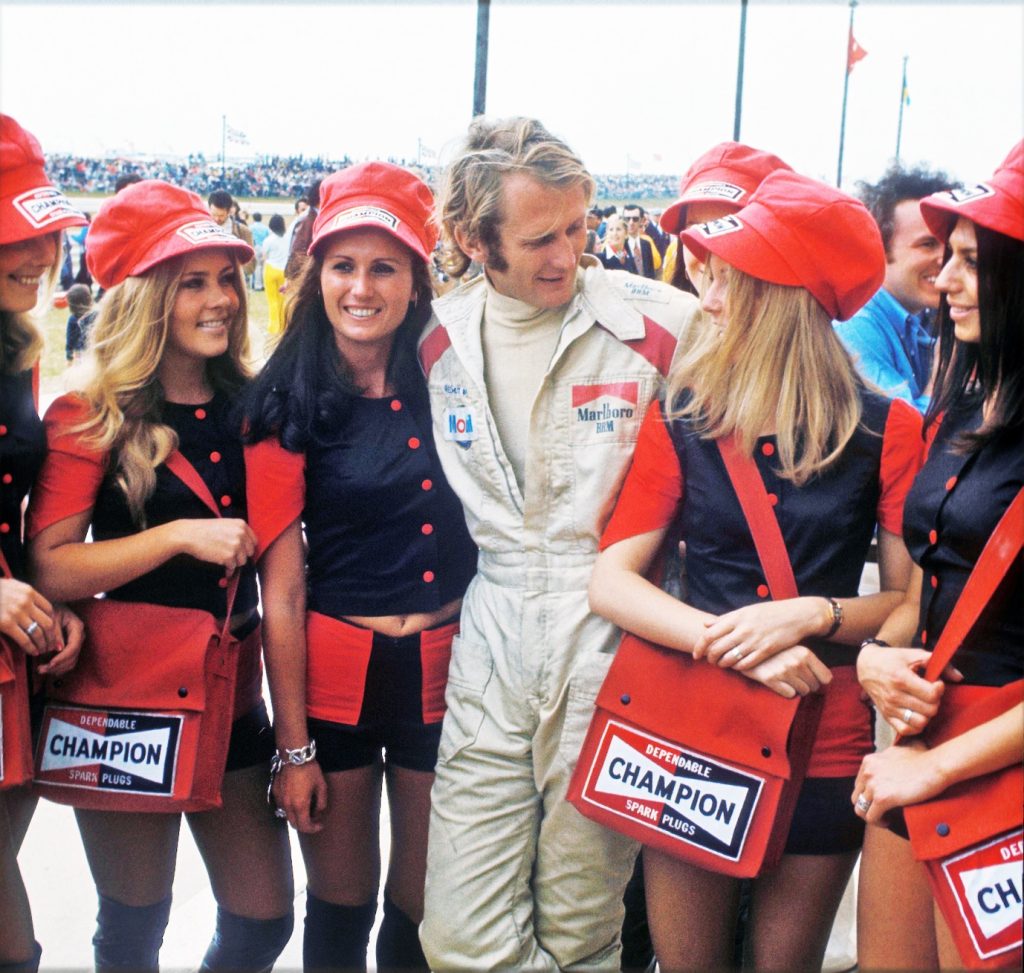 Racing driver Helmut Marko with 6 girls with red caps, blue tops and "Champion" bags